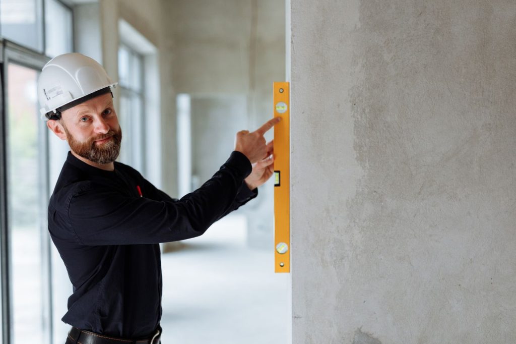 an-engineer-holding-a-spirit-level-against-a-wall-8482824 Confident engineer with hard hat using a spirit level on a wall at a construction site.