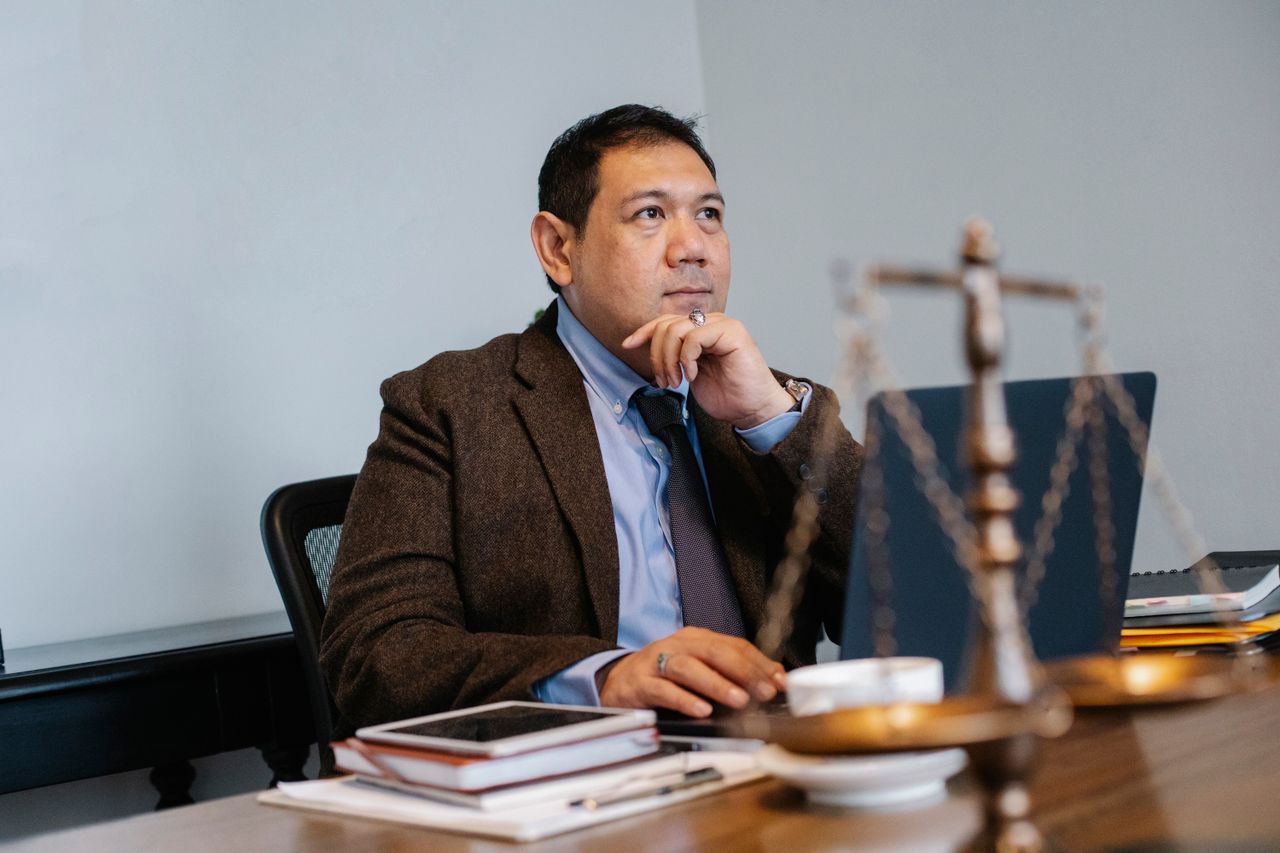 Crafting Captivating Headlines: Your awesome post title goes here Pensive Asian male lawyer in formal suit browsing netbook while sitting at table with decorative scale of justice and touching chin in contemplation