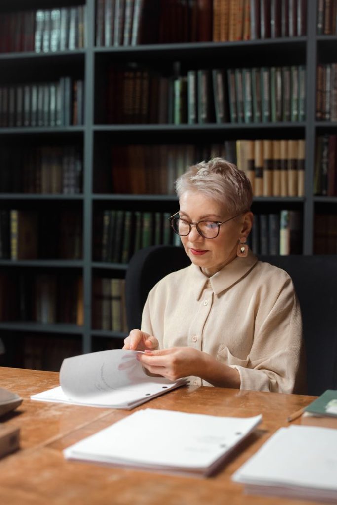 professional-drama-professor-looking-at-a-script-7967581 Elderly woman analyzing scripts in a library, highlighting expertise.